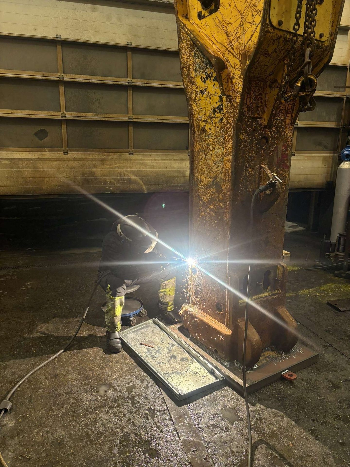 Mekaniker sveiser på en hydraulisk hammer i verkstedet